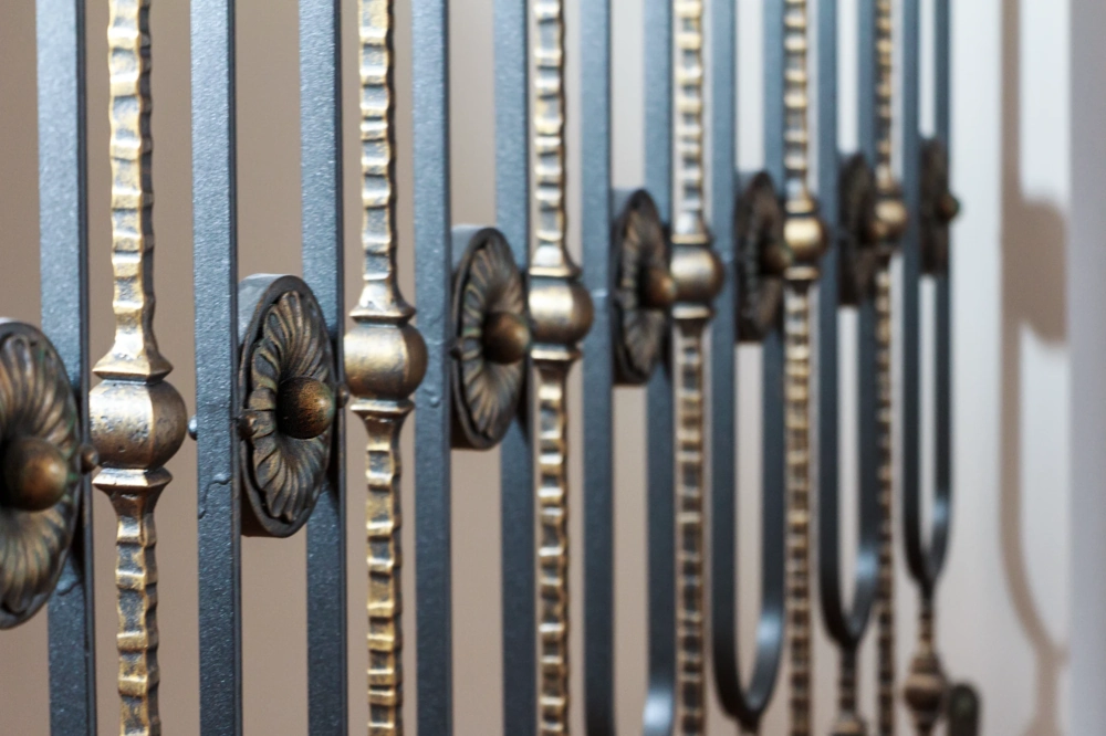 Fragment ogrodzenia kutego z ozdobnymi metalowymi rozetami i pionowymi prętami