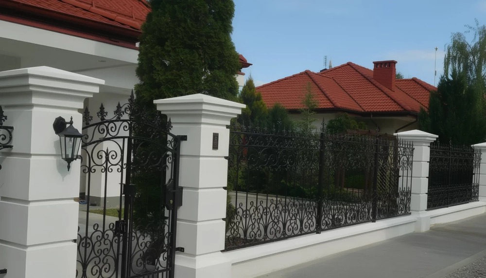 Ogrodzenia kute z metalową furtką i białymi słupkami
