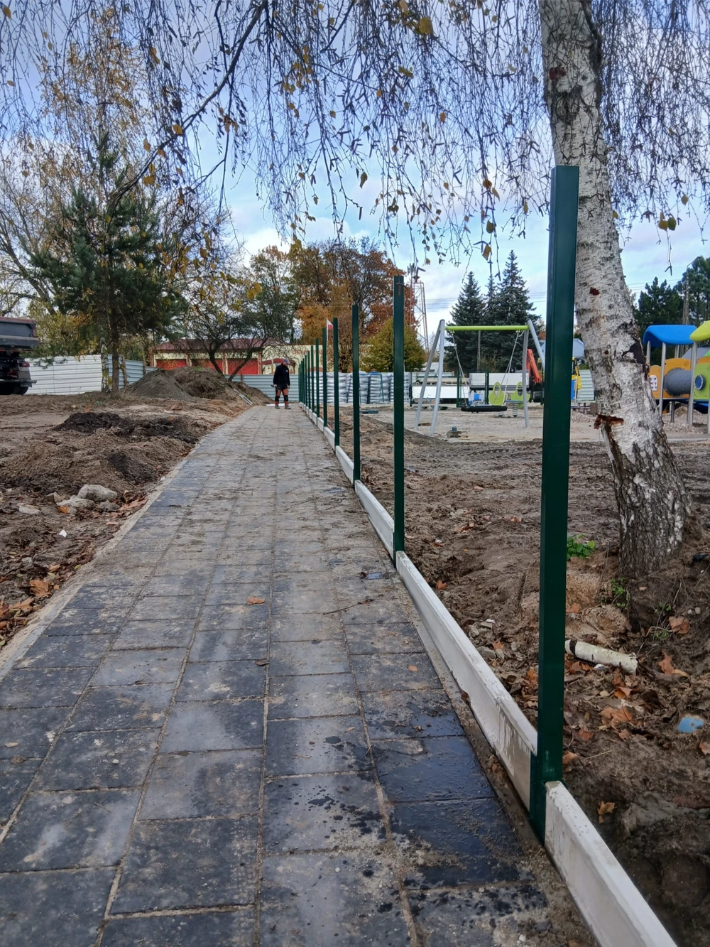 Montaż ogrodzenia panelowego – wzdłuż kamiennej ścieżki osadzone stalowe słupki i dolna belka