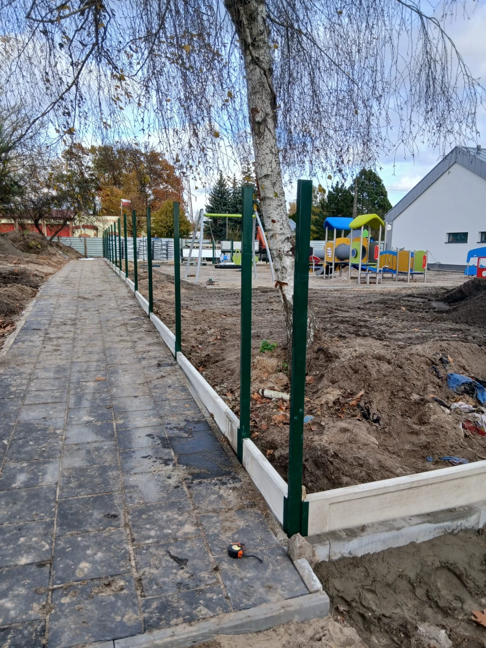 Montaż ogrodzenia panelowego 2d – zielone słupki i betonowe przęsła na podmurówce przy chodniku