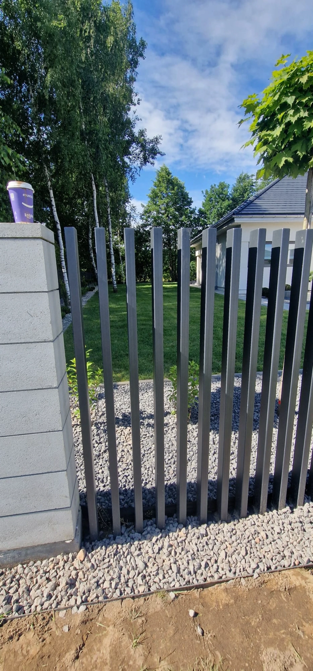 Ogrodzenie palisadowe z aluminiowych pionowych przęseł osadzone na podmurówce z bloczków i dekoracyjnym grysie