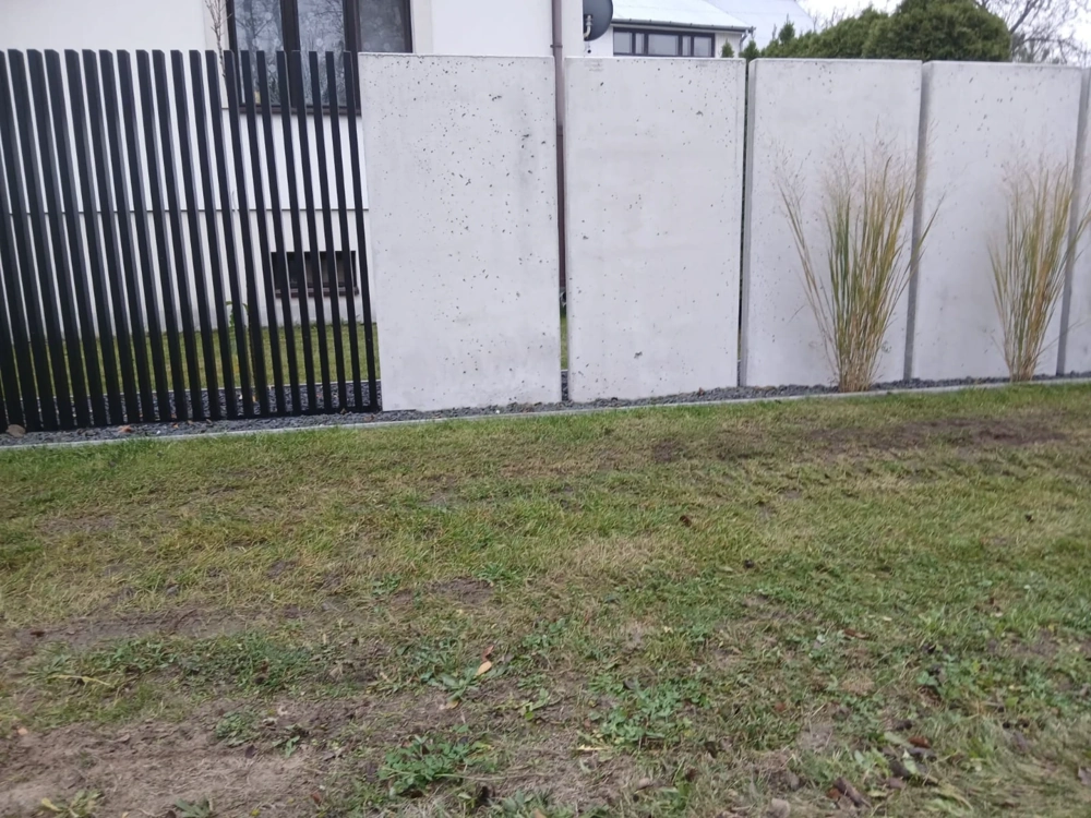 Ogrodzenia betonowe z gładkimi panelami betonowymi i czarnymi, pionowymi panelami metalowymi na trawniku